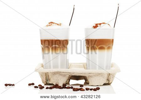 dva latte macchiato s čokoládovým práškem v cupholder s kávová zrna a lžíce