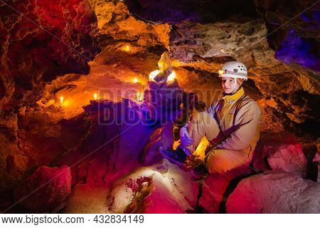 Women Explore The Beautiful Stone Cave Mlynky In Ukraine. Multicolored Light Shines On The Stones. E