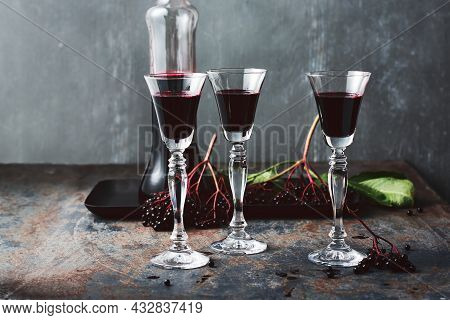 Homemade Elderberry Liqueur In Glasses And A Bottle, Ripe Elderberries.