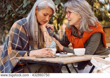 Careful Senior Woman Calms Dowm Sad Asian Friend Spending Time Together In Street Cafe