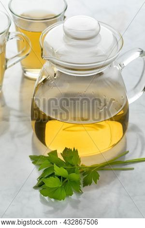Glass teapot with lovage tea and a fresh twig of lovage in front 