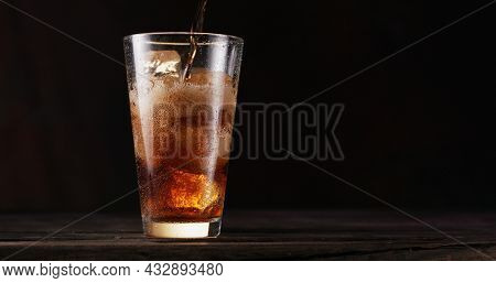 uring the liquid into the cola glass full of ice cubes. Isolated on dark background.