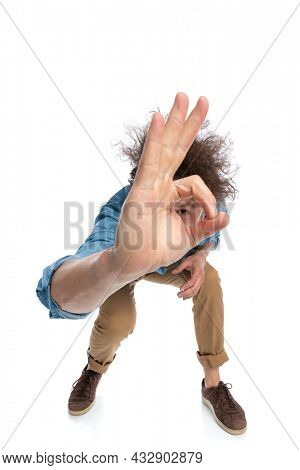 young casual man leaning forward and peeking through the finger hole on white background