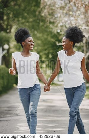 Twin Afro-american Sisters Holding Hands And Walking In A Park