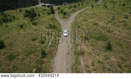 Aerial View Of A Passenger White Car Driving On A Rural Narrow Road In Mountains. Action. A Vehicle 