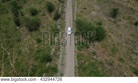 Aerial View Of A Passenger White Car Driving On A Rural Narrow Road In Mountains. Action. A Vehicle 