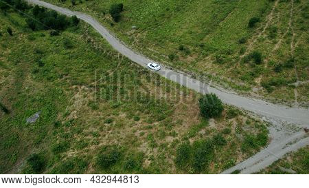 Aerial View Of A Passenger White Car Driving On A Rural Narrow Road In Mountains. Action. A Vehicle 