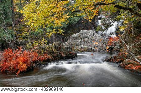 Large rocks in running water of Dead river surrounded with fall foliage in Michigan upper peninsula.