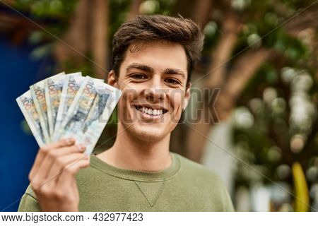 Young hispanic man smiling happy holding peruvian soles banknotes at the city.