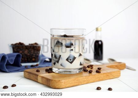 Glass Of Milk With Grass Jelly And Coffee Beans On White Wooden Table