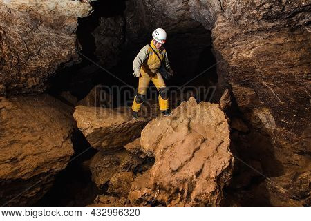 Tourist In A Protective Suit And Helmet With A Flashlight Explores The Cave. Extreme Active Sport