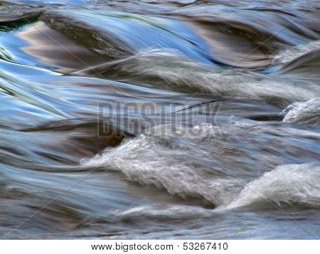 Flowing water with the reflection of the blue sky taken with a slow shutter speed 	