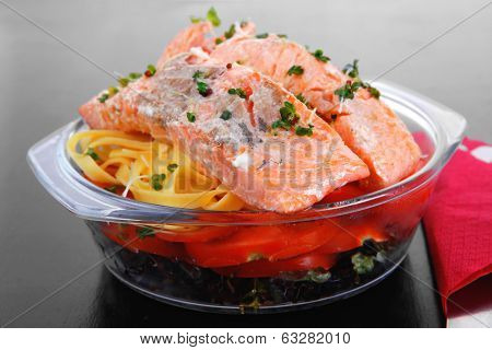 fresh fried natural pink salmon on italian traditional tagliatelle backed with tomato and vegetables served over black wooden table