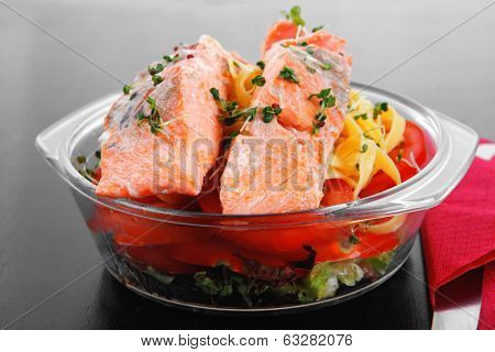 fresh fried natural pink salmon on italian traditional tagliatelle backed with tomato and vegetables served over black wooden table