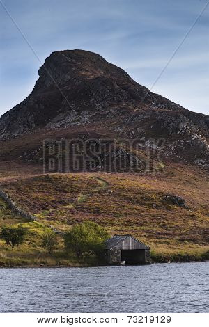 Landscape Of Steep Hill Peak With Small Boathouse On Lake In Foreground