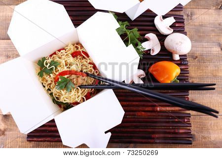 Chinese noodles in takeaway boxes on bamboo mat on wooden background