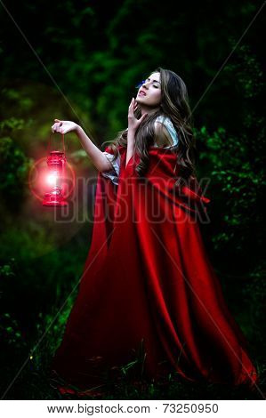 beautiful woman with red cloak and lantern in the woods by night