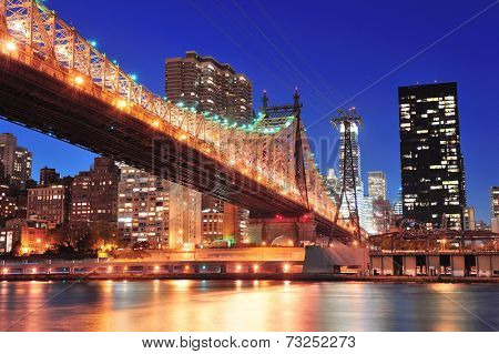 Queensboro Bridge over New York City East River at sunset with river reflections and midtown Manhattan skyline illuminated. 