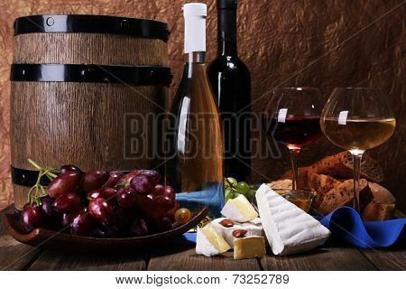 Supper consisting of Camembert and Brie cheese, honey wine and grapes on napkin in basket and wine barrel on wooden table on brown background