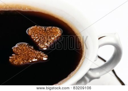 Two cubes of heart-shaped sugar floating in a cup of coffee