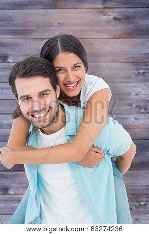 Happy casual man giving pretty girlfriend piggy back against faded grey wooden planks