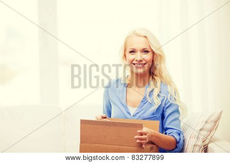 transportation, post and people concept - smiling young woman opening cardboard box at home