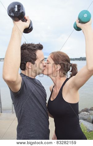 A Young, caucasian couple working out with dumbbells outside
