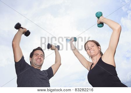 A Young, caucasian couple working out with dumbbells outside