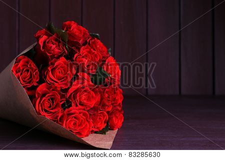 Bouquet of red roses wrapped in paper on wooden background