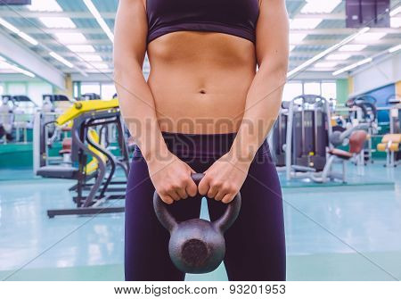 Woman with slim waist and black sportswear holding kettlebell