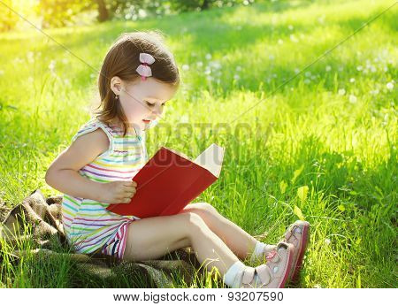 Child Reading A Book On The Grass In Sunny Summer Day