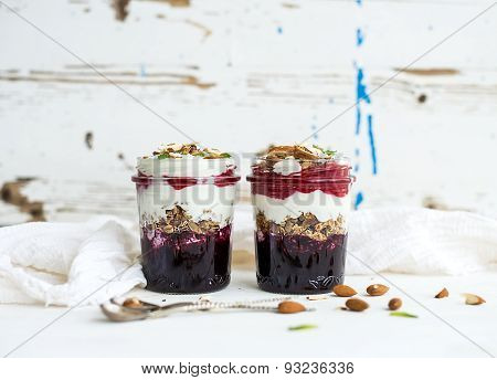 Yogurt oat granola with berries, honey and nuts in glass jars, rustic white  background