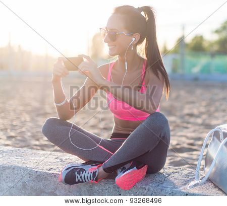 Athlete woman taking picture with smartphone camera, listining music, chatting on the beach summer h
