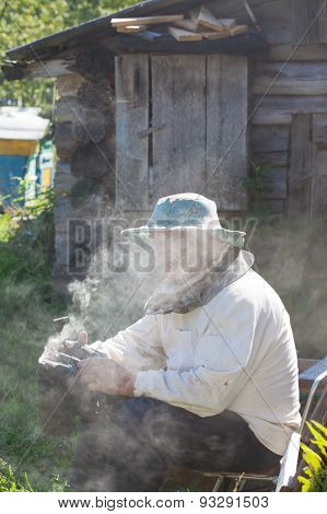 Bee-keeper In A Protective Suit With Bee Smoker For Smoking Of Bees