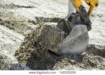Excavator in a situation digs holes in the sandy ground.