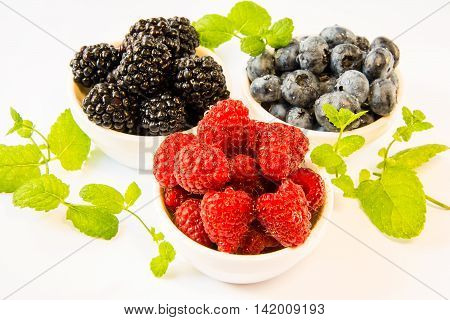 raspberries blackberries blueberries in white plates with mint on a white table