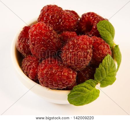 raspberries in a white plate with mint on a white table