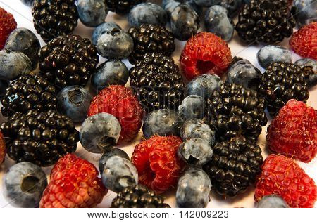 raspberries blackberries blueberries on a white table