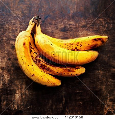 A branch of rotten ripe bananas on vintage wooden background. Overripe banana close up