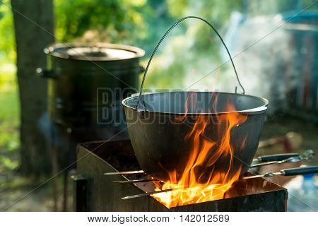 Cooking in sooty bowler on campfire at forest during hike