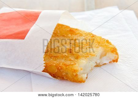 Single Partially Eaten Hash Brown In Paper Bag On White Napkin.