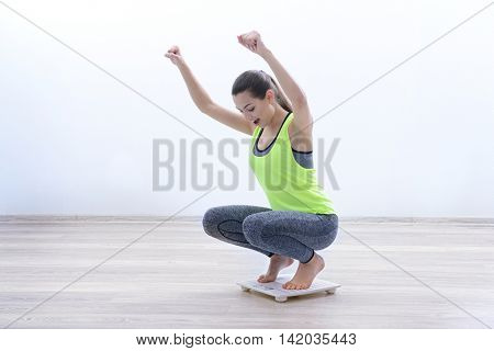 Woman celebrating a weightloss goal achievement on a scale at home