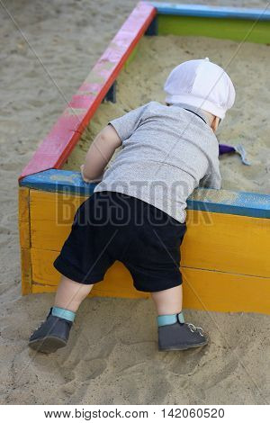 Kid playing on the Playground in the warm time of the year. The child digging in the children's sandbox. Rear view.