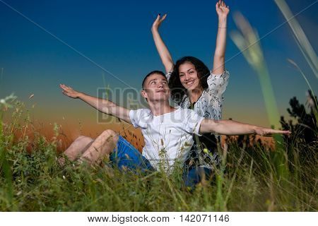 young romantic couple open arms and having fun at sunset on outdoor, beautiful landscape and dark sky, love tenderness concept, young adult people
