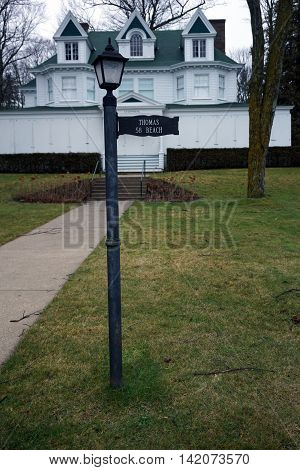 WEQUETONSING, MICHIGAN / UNITED STATES - DECEMBER 22, 2015: A lamppost, with an attached sign indicating the house number and owner's name, stands in front of a large white home, christened Cedarmere, on Beach Road in Wequetonsing.