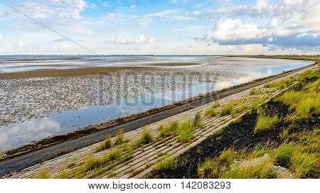 Bended embankment next to a Dutch estuary at low tide on an early morning in the summer season.