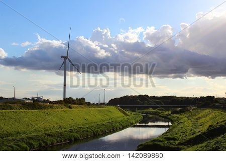 A wind turbine in a peaceful landscape with green grass blue skye and a river