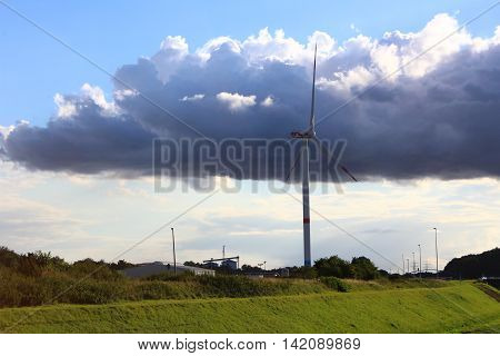 A wind turbine in a peaceful landscape with green grass blue skye and a river