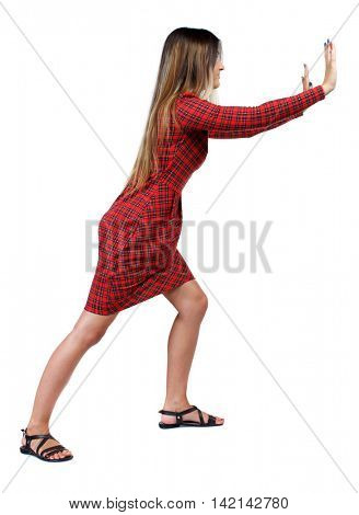 back view of woman pushes wall.  Isolated over white background. Rear view people collection. backside view of person. The girl in red plaid dress stands sideways and pushing his hands something to