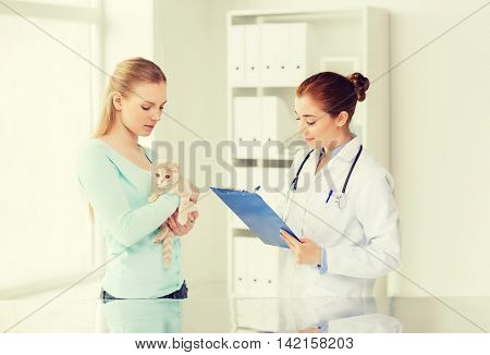 medicine, pet, animals, health care and people concept - woman holding scottish fold kitten and veterinarian doctor with clipboard at vet clinic